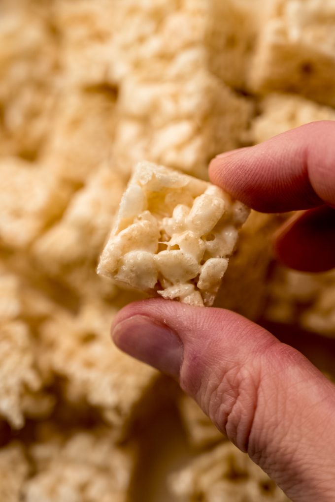 Someone is holding a small cube of chopped Rice Krispies treats.