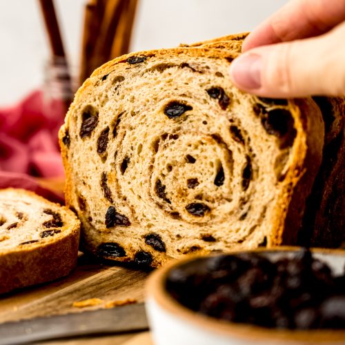Someone is grabbing a slice of cinnamon raisin bread from a surface.