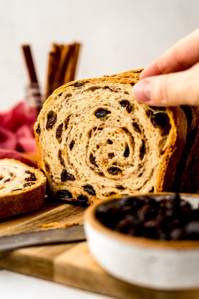 Someone is grabbing a slice of cinnamon raisin bread from a surface.