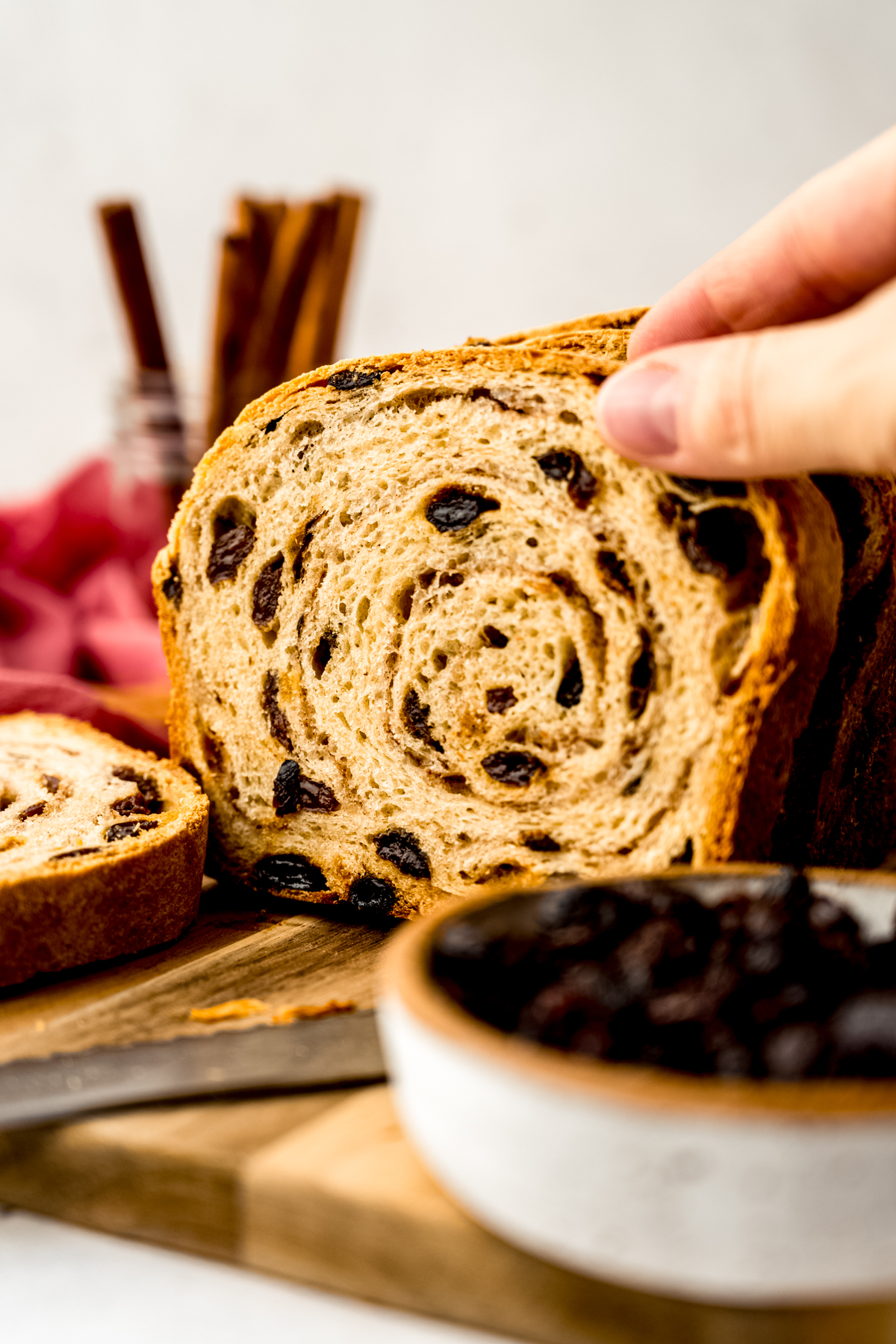 Someone is grabbing a slice of cinnamon raisin bread from a surface.