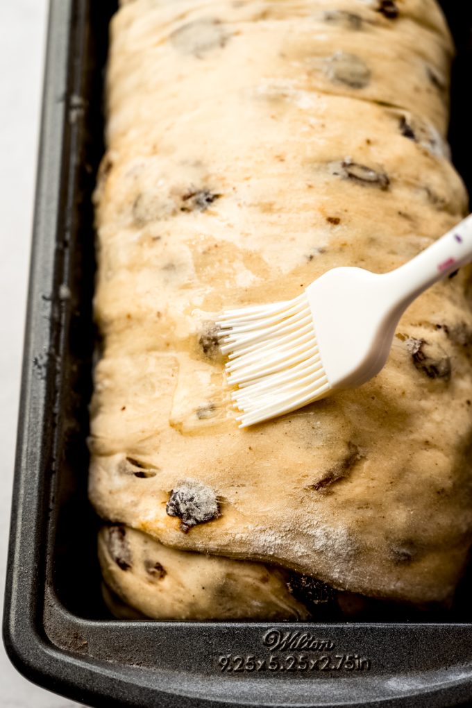 Someone is brushing cinnamon raisin bread dough with melted butter before baking.