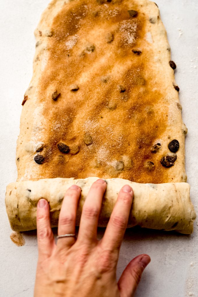 Someone is rolling up a rectangle of cinnamon raisin bread dough.