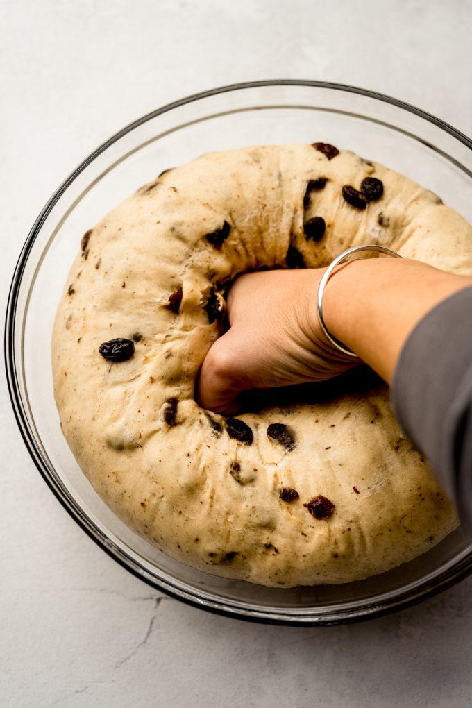 Someone is punching down cinnamon raisin bread dough in a glass bowl.