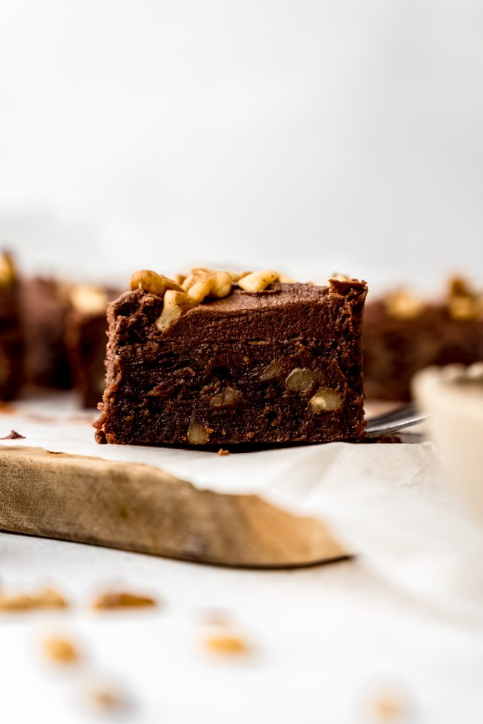 A frosted brownie with walnuts on a cutting board.