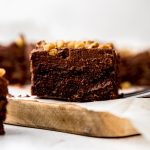 A frosted brownie with walnuts on a cutting board.