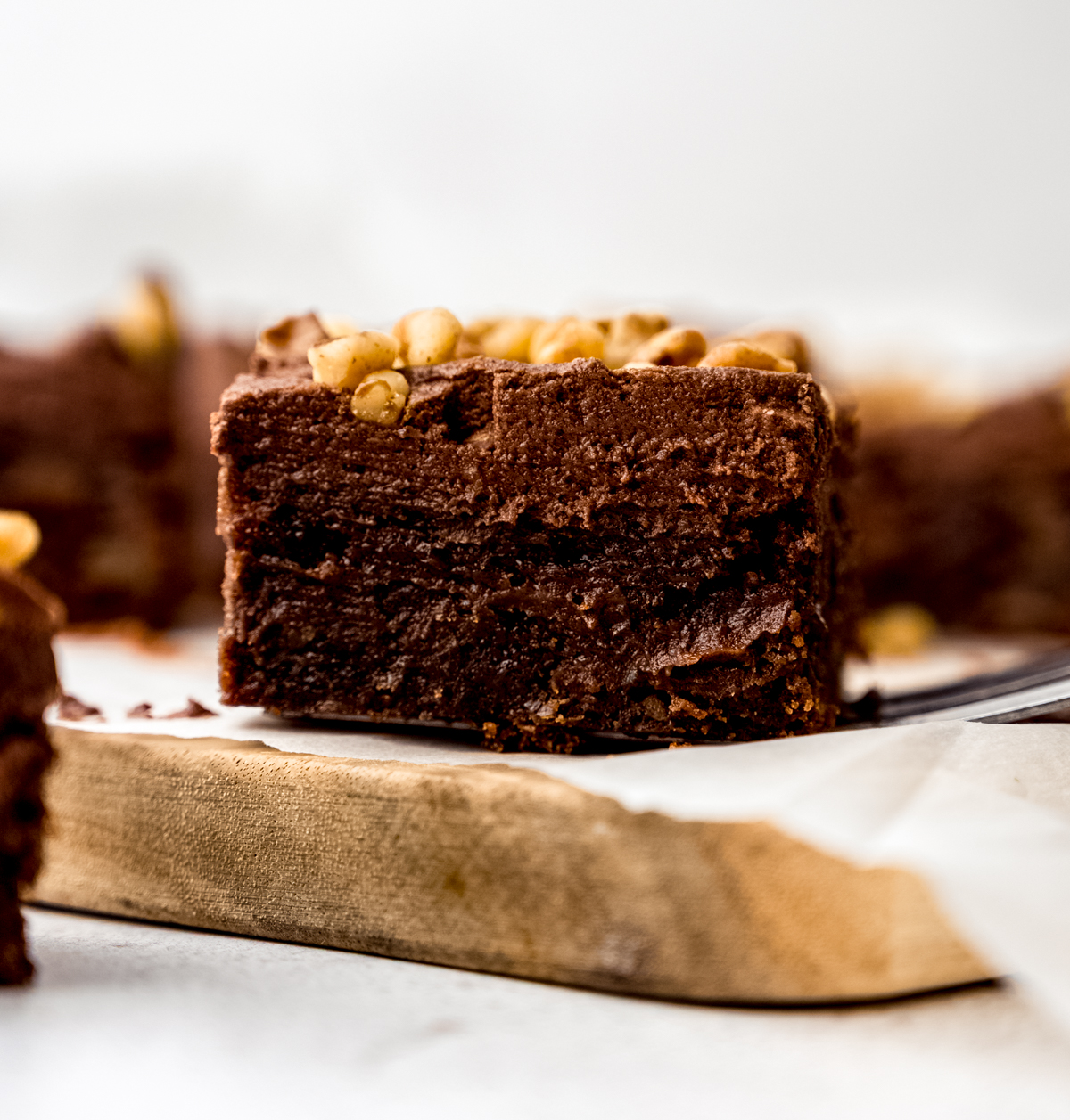 A frosted brownie with walnuts on a cutting board.