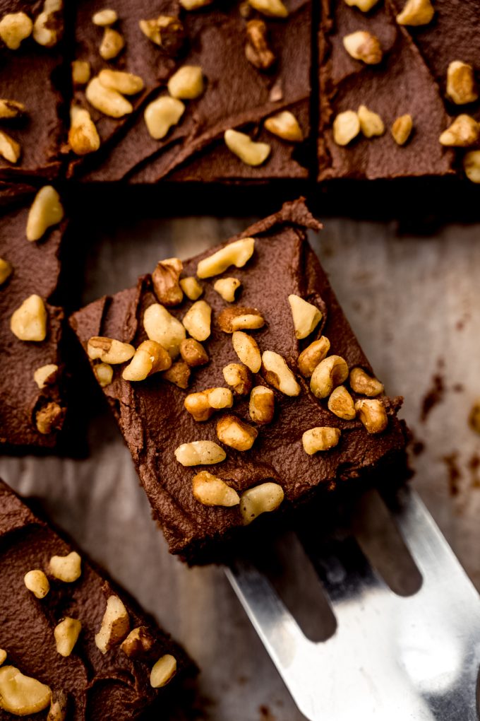 Someone is using a spatula to serve a frosted brownie with walnuts.