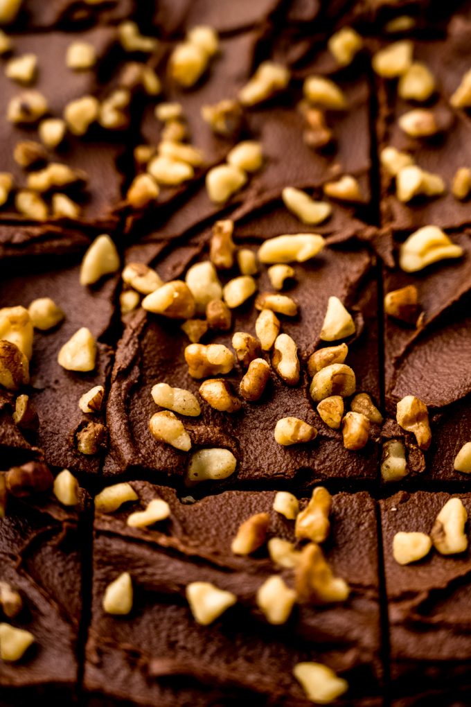 Frosted brownies with walnuts on a surface.