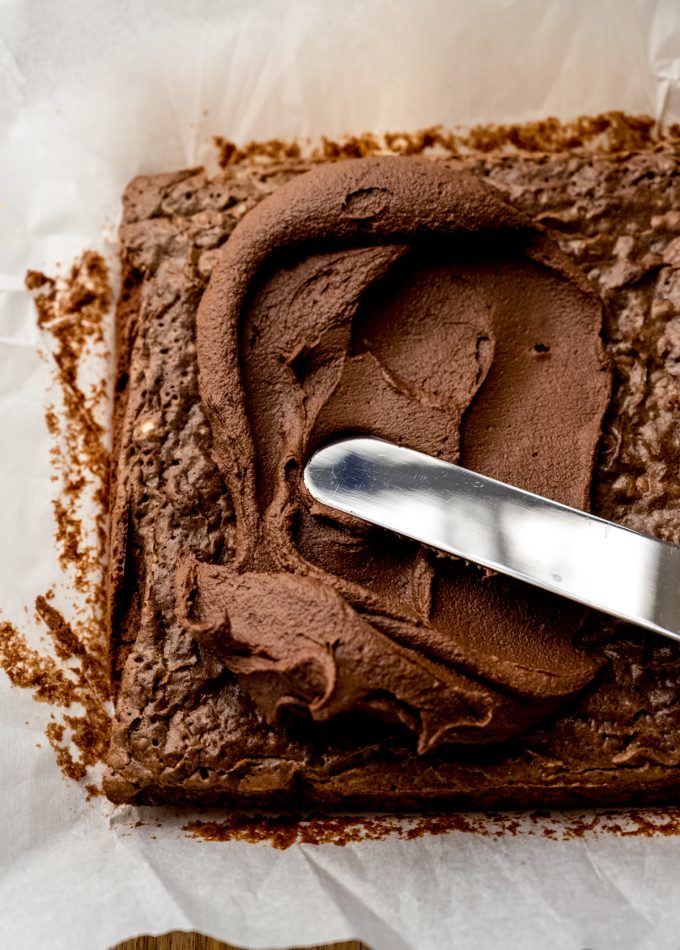 Someone is using a spatula to spread chocolate frosting onto brownies.