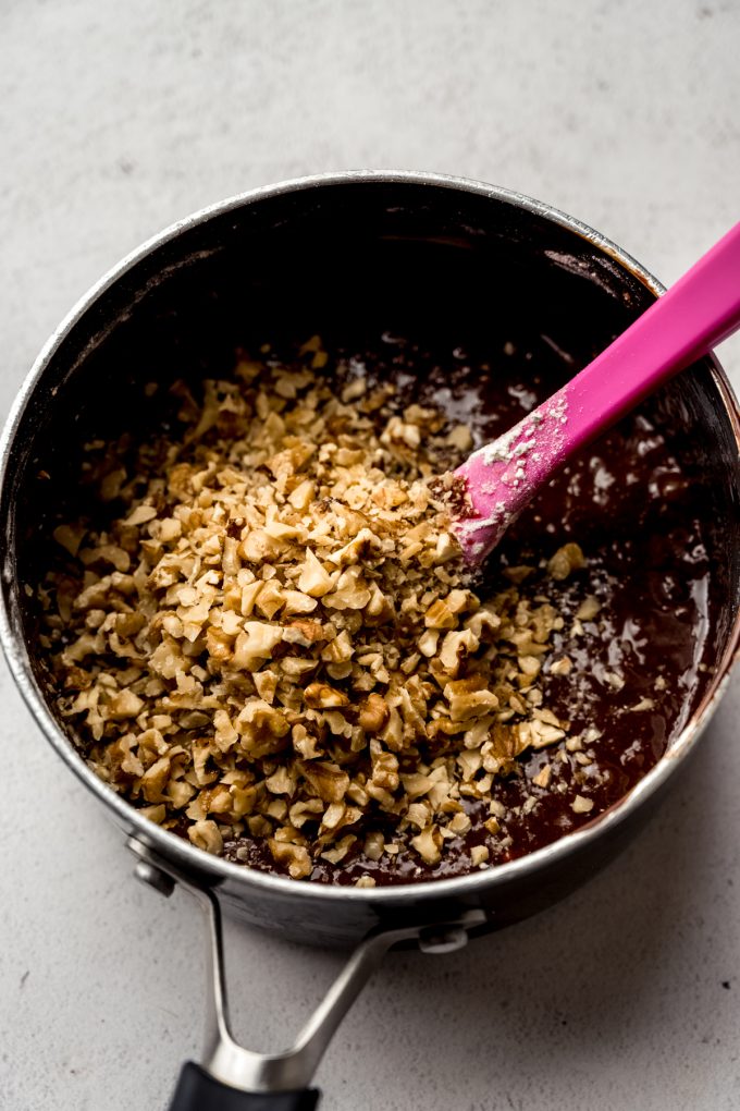 A saucepan with brownie batter that has chopped walnuts poured into it getting ready to stir.