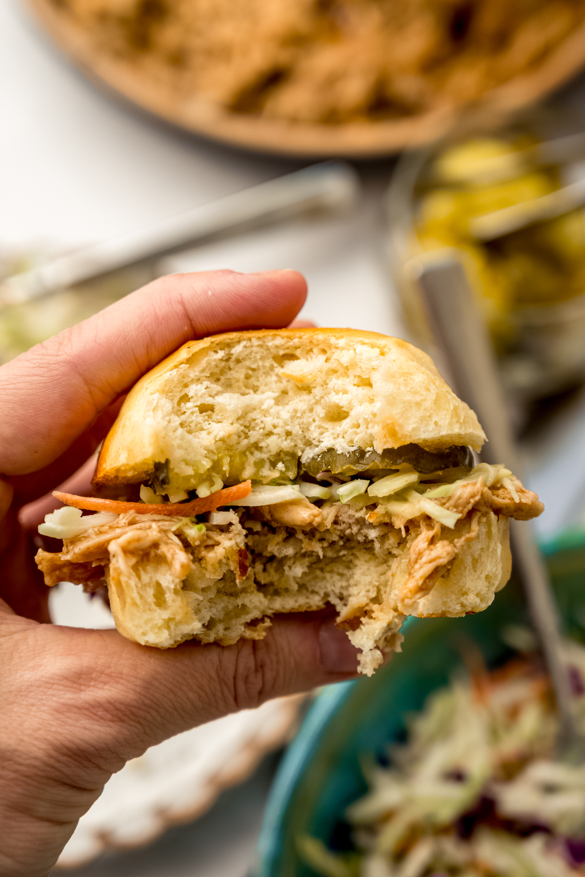 Someone is holding a slider sandwich with a bite taken out of it.