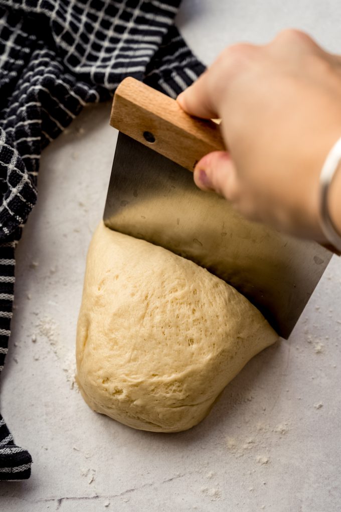 Someone is using a bench scraper to portion dough into individual rolls.