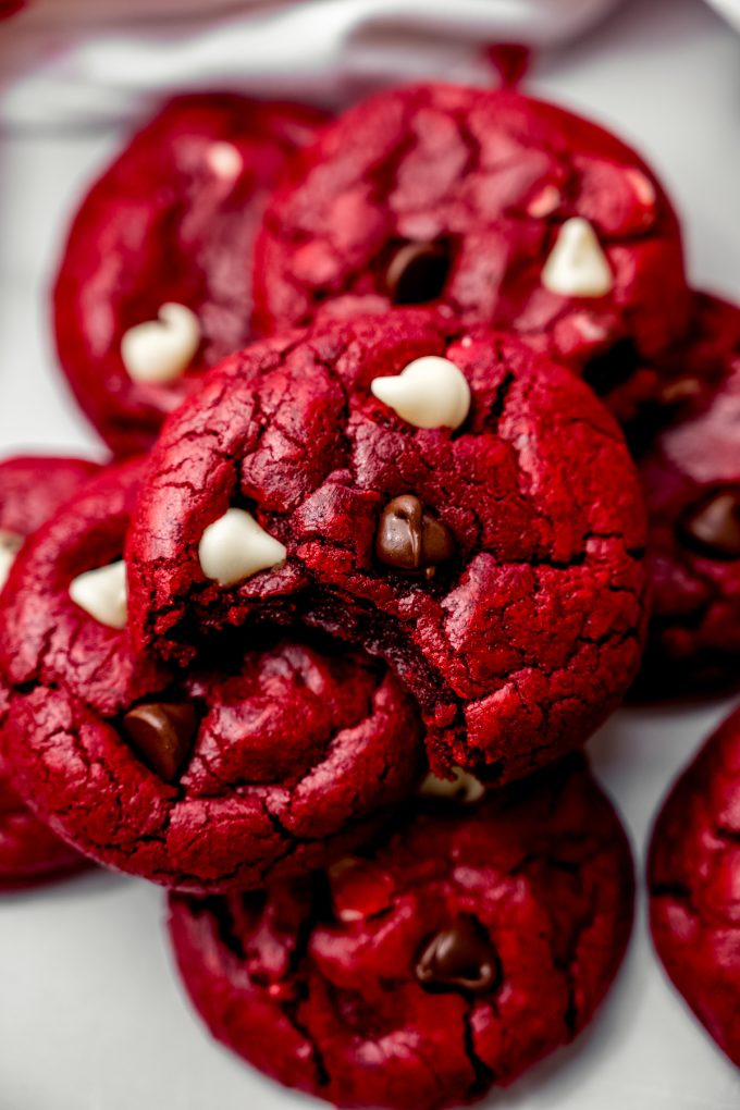Aerial photo of red velvet chocolate chip cookies on a plate and the one on the top has a bite taken out of it.