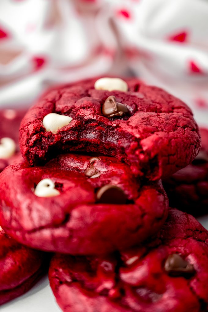 Red velvet chocolate chip cookies on a plate and the one on the top has a bite taken out of it.