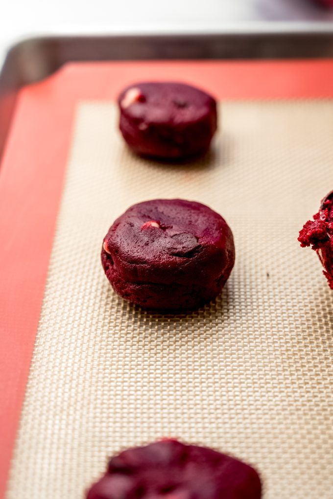 A disc of red velvet chocolate chip cookie dough on a baking sheet.
