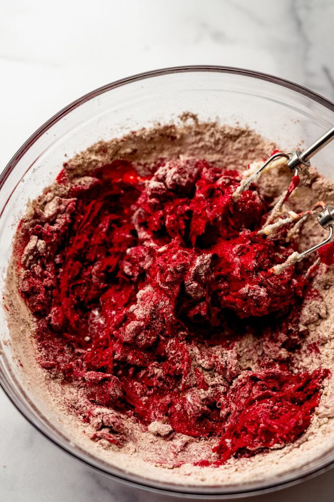 Red velvet chocolate chip cookie dough coming together with a hand mixer in a bowl.