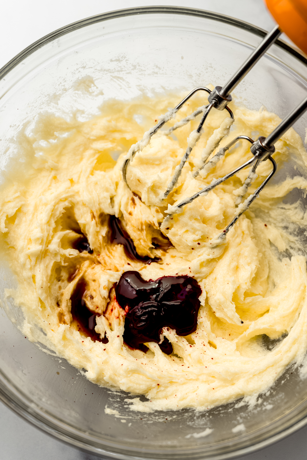Creamed butter and sugar in a bowl with vanilla extract and red food coloring ready to blend in with the electric mixer beaters.