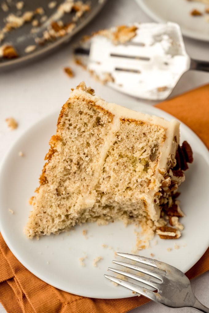 A slice of butter pecan cake on a plate with a bite taken out of it.