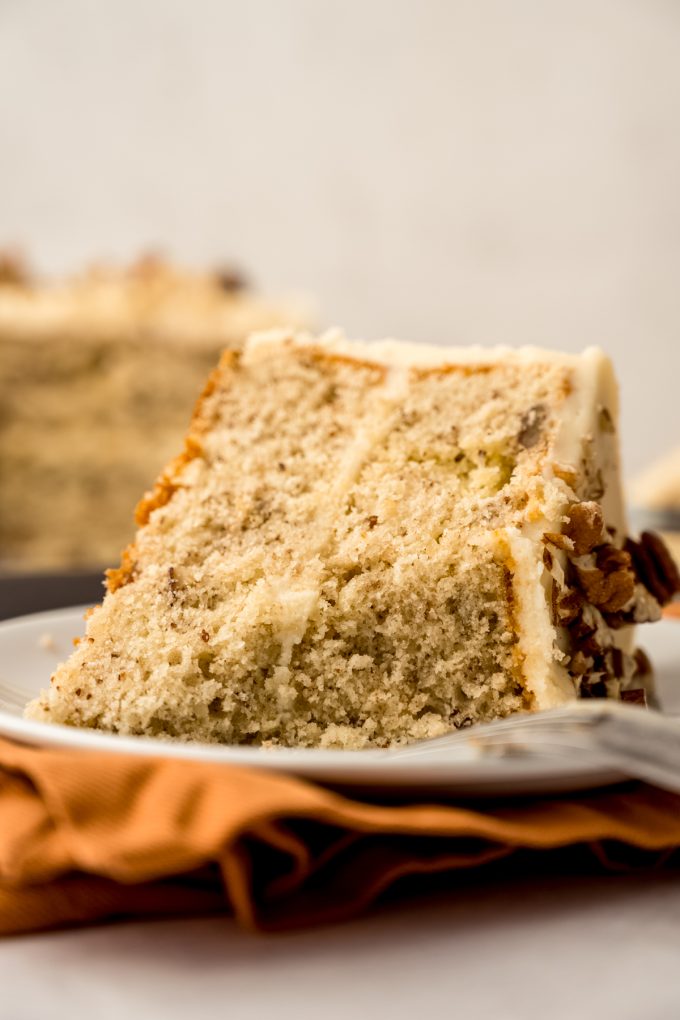 A slice of butter pecan cake on a plate with a bite taken out of it.