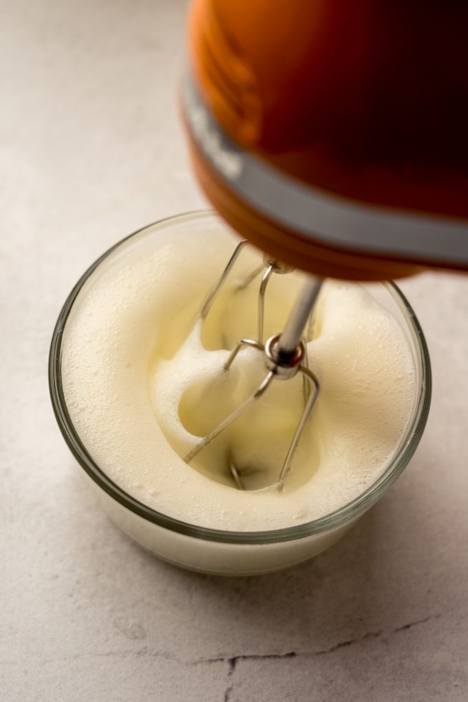 Someone is whipping egg whites in a small glass bowl with a handheld mixer.