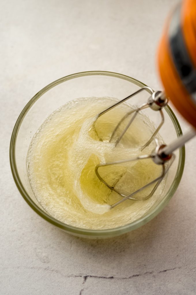 Someone is whipping egg whites in a small glass bowl with a handheld mixer.