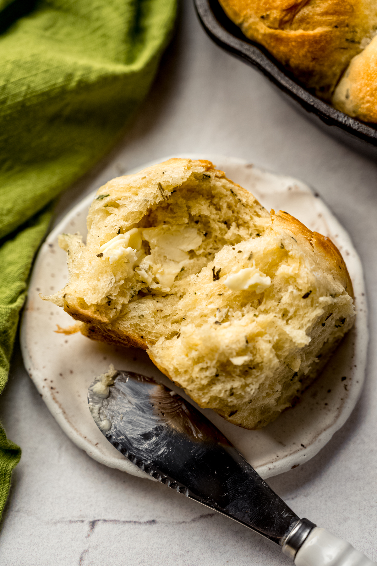An herbed skillet roll that has been spread with butter on a plate with a spreader.
