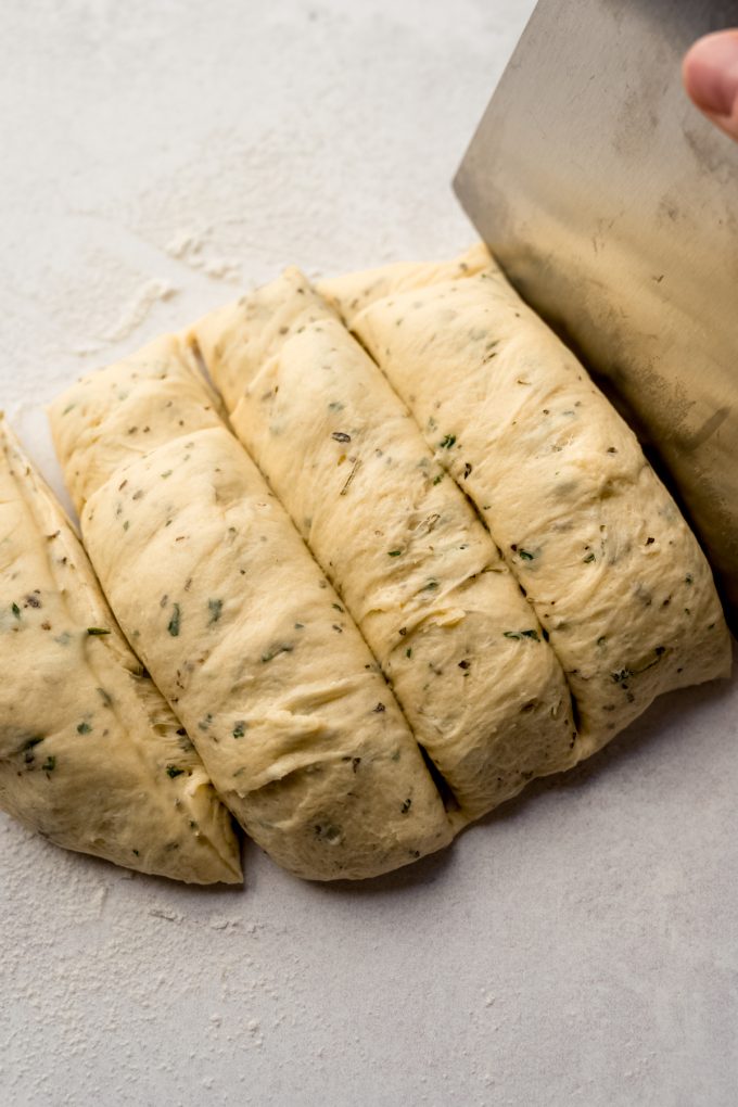 Someone is cutting herbed dinner roll dough with a bench scraper.