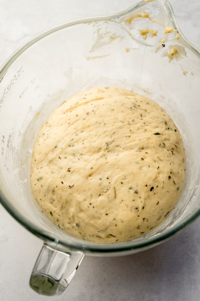 Herbed dinner roll dough that has rise in a glass bowl.