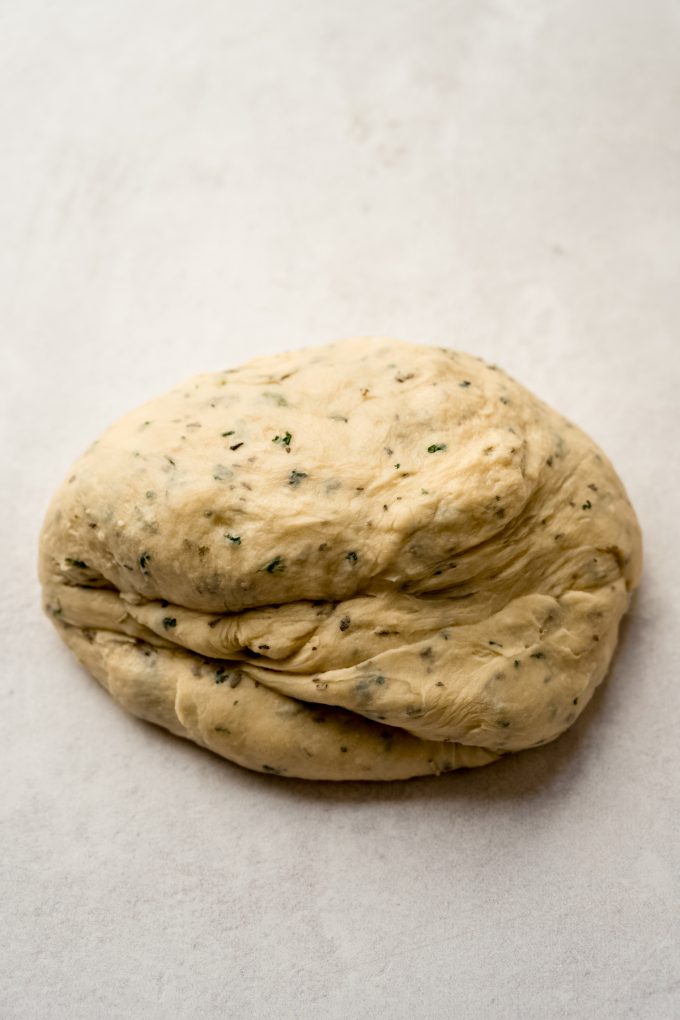 A ball of herbed dinner roll dough on a surface.