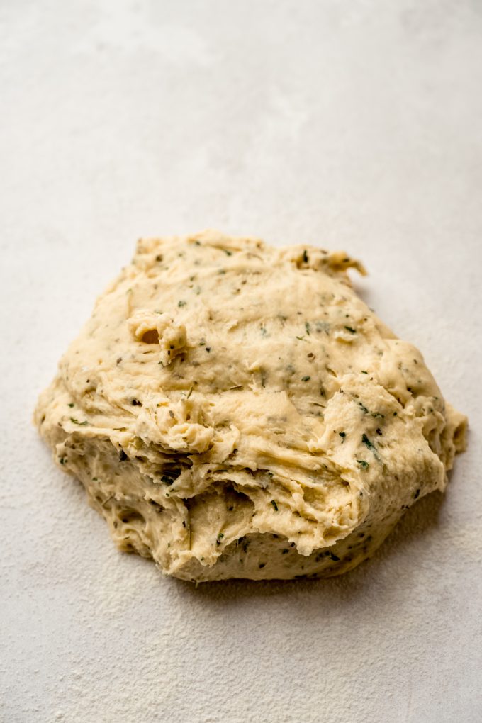 A ball of herbed dinner roll dough on a surface before it has been kneaded.