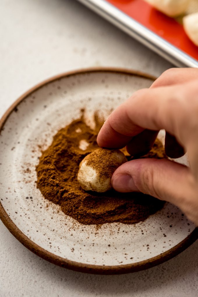 Someone is using their fingers to roll an Irish potato candy in cinnamon.