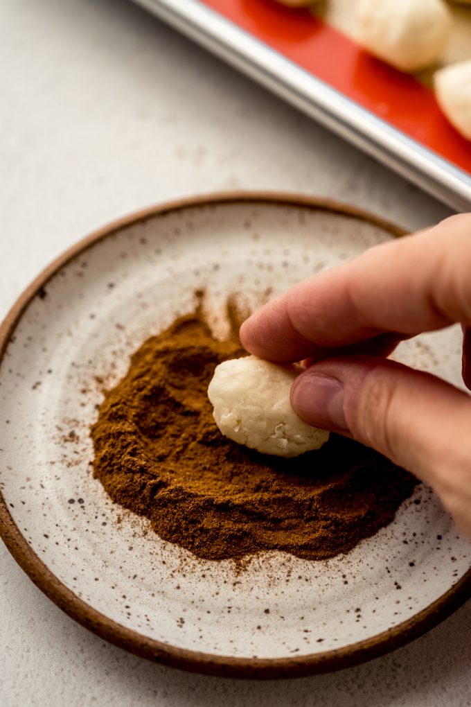 Someone is using their fingers to roll an Irish potato candy in cinnamon.