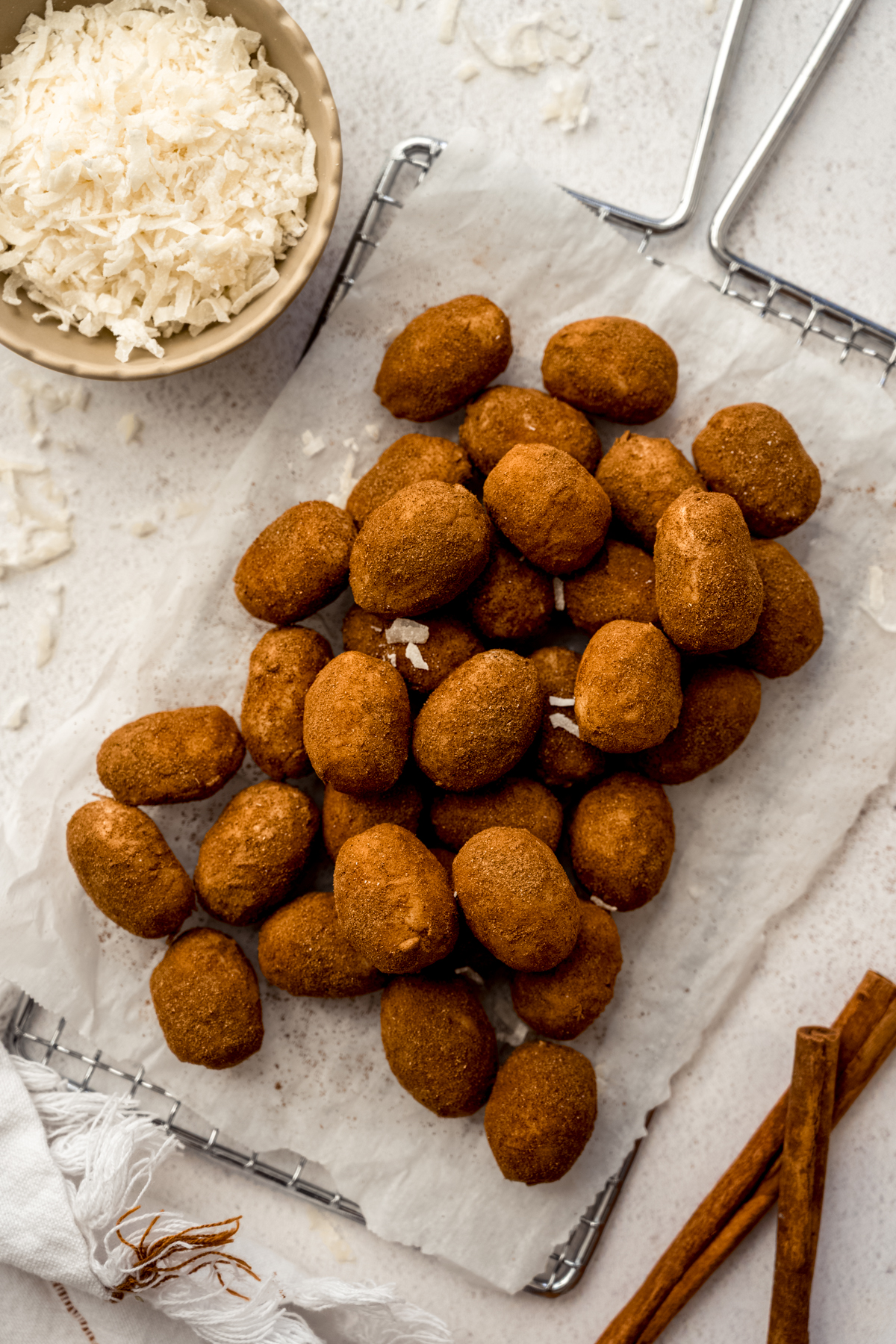 Aerial photo of Irish potato candy on a surface with a bowl of shredded coconut and cinnamon sticks around it.