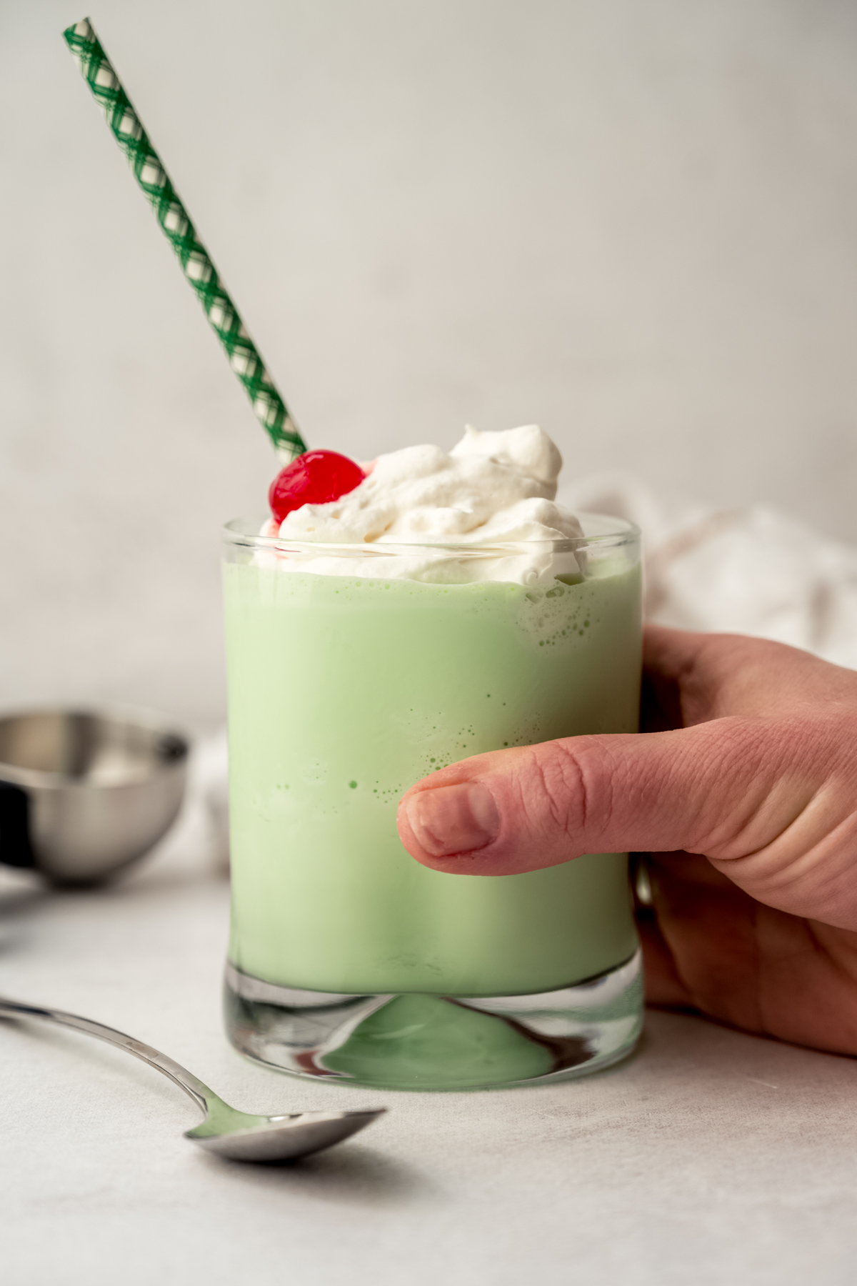 A glass with a homemade Shamrock Shake in it and someone's hand is around the glass.
