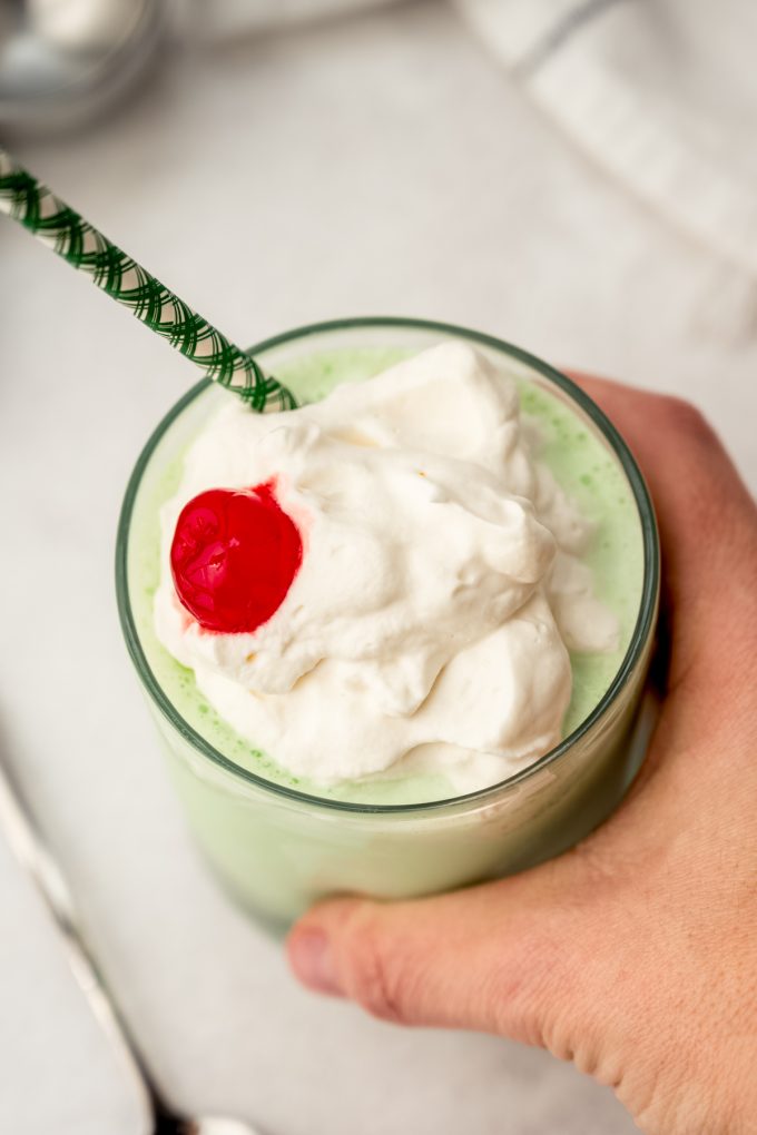 A glass with a homemade Shamrock Shake in it and someone's hand is around the glass.