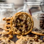 Sourdough discard chocolate chip cookies on a cooling rack with jars behind it.