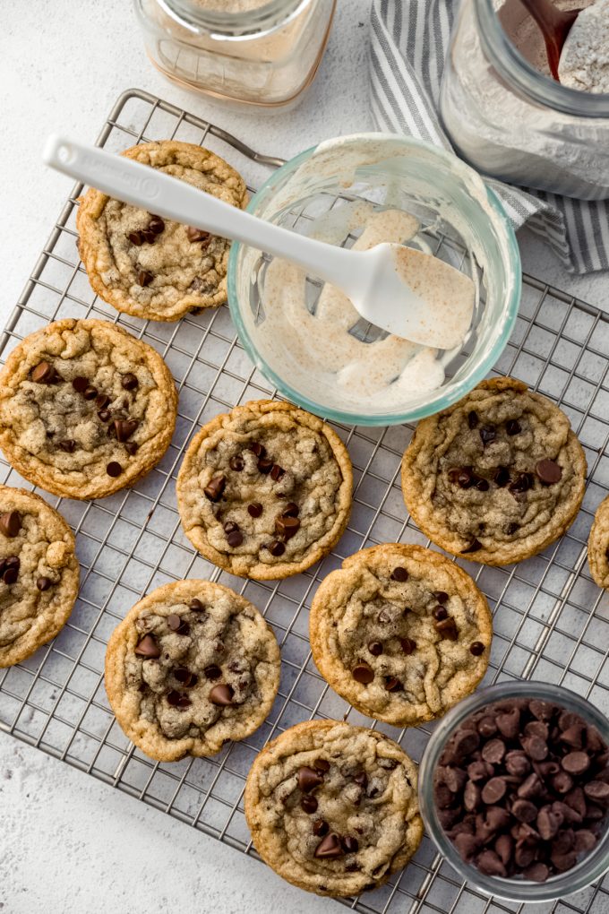 Aerial photo of sourdough chocolate chip cookies on a cooling rack with a bowl of discard with a spatula in it.