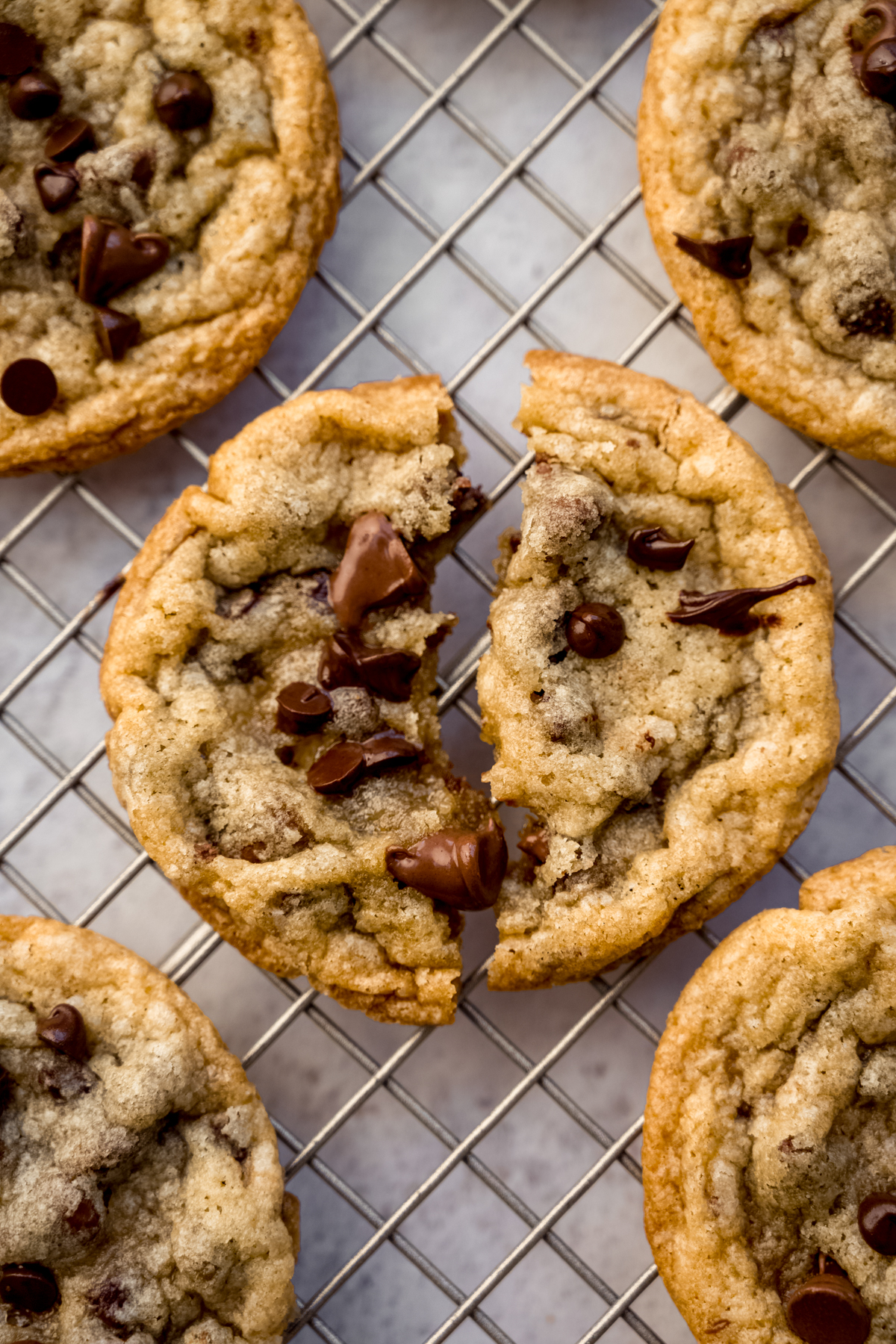 Aerial photo of sourdough chocolate chip cookies on a cooling rack and one has been broken in half.