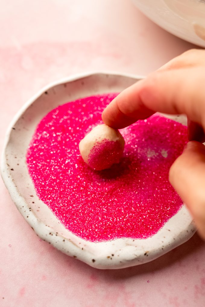 Someone is rolling a strawberry truffle in pink sanding sugar.