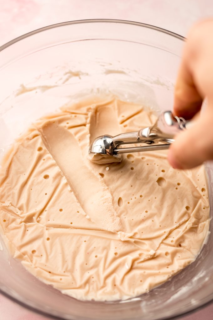 Someone is using a scooper to scoop strawberry truffle filling from a bowl.