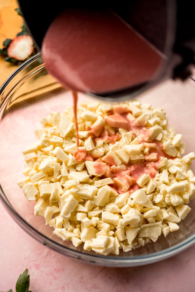 Someone is pouring strawberry puree over a bowl of white chocolate chunks to make strawberry truffles.