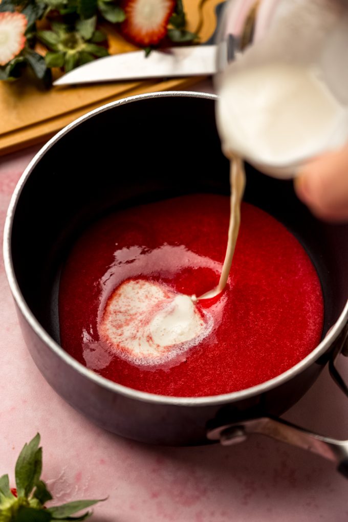 Someone is pouring cream into a saucepan of strawberry puree.