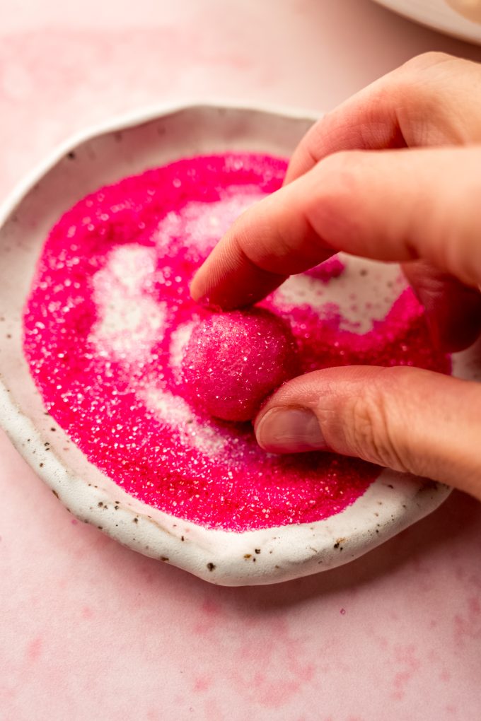 Someone is rolling a strawberry truffle in pink sanding sugar.