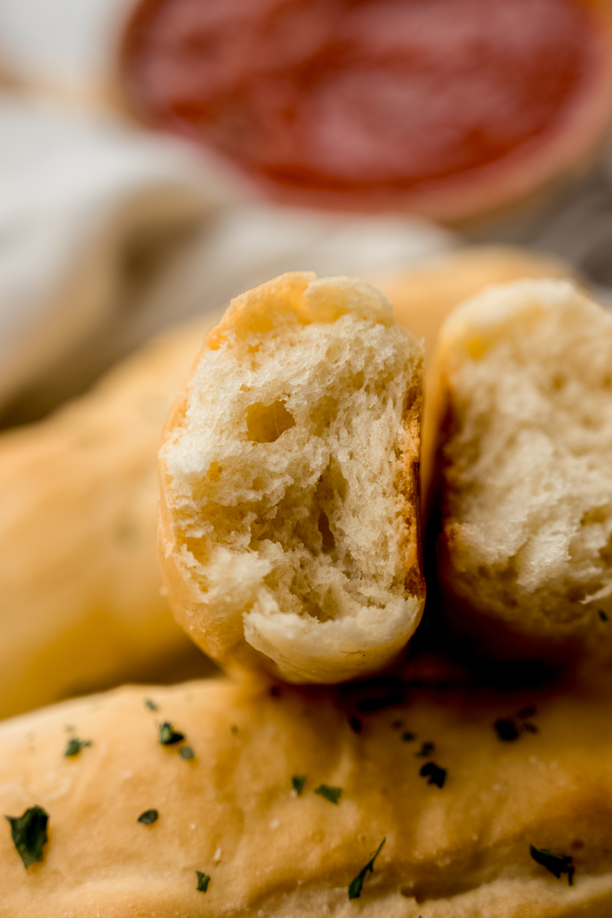 Breadsticks on a surface and one is broken in half so you can see the inside crumb.