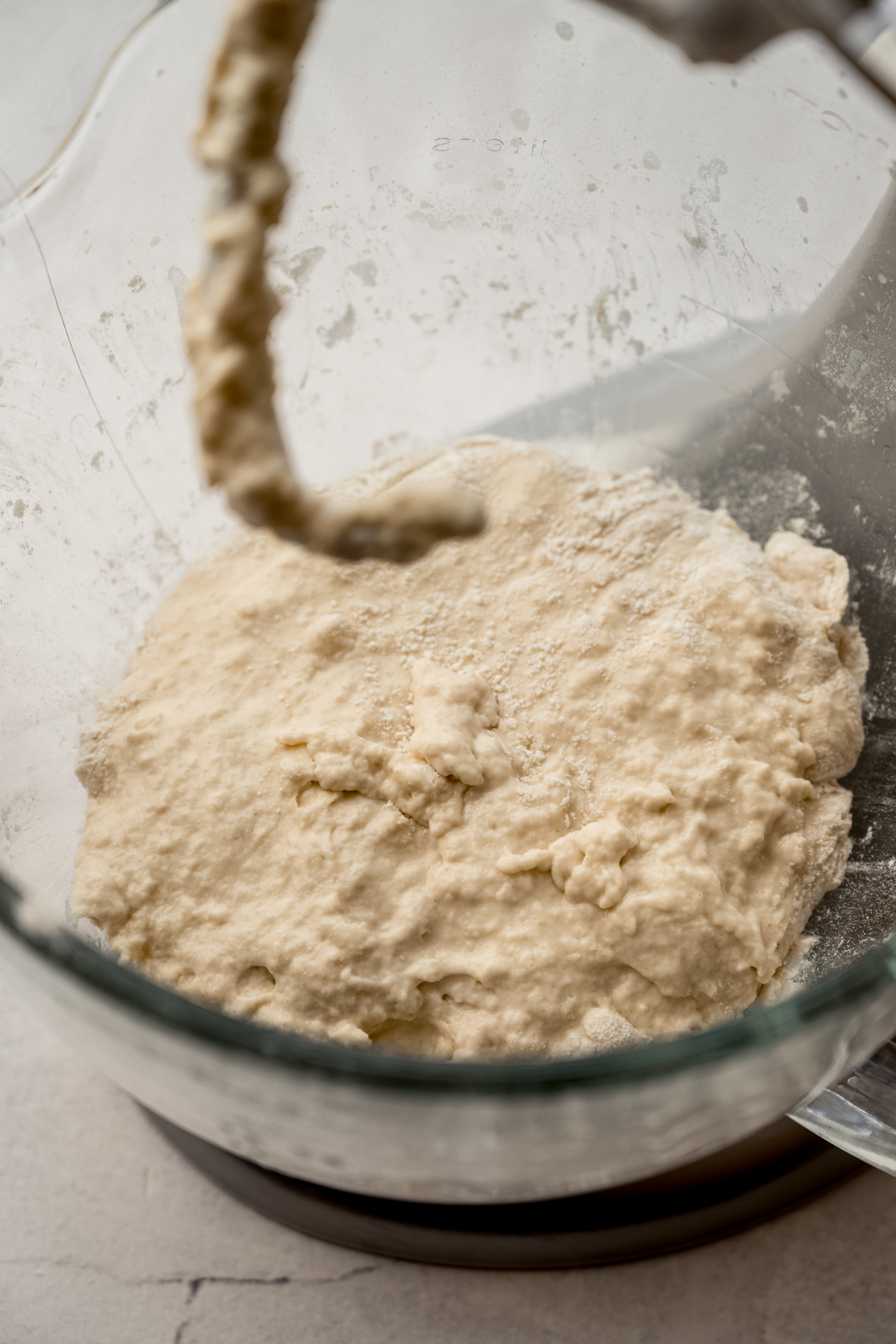 The dough of a yeast bread coming together in the bowl of a stand mixer with a hook attachment.