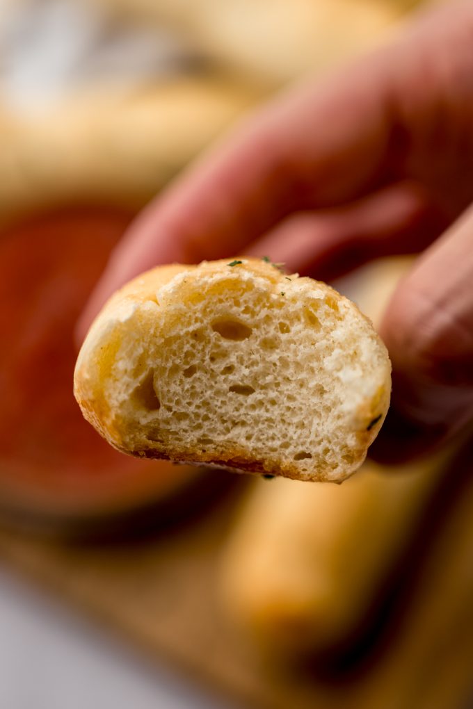 Someone is holding a breadstick that has a bite taken out of it.