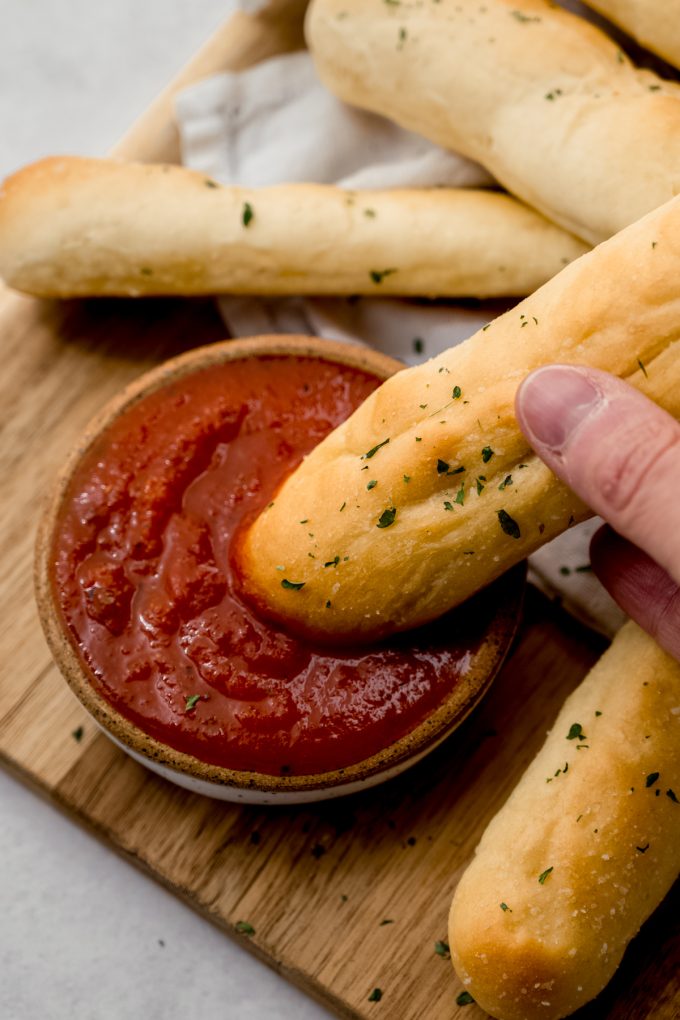 Someone is dipping a homemade garlic breadstick into marinara sauce.