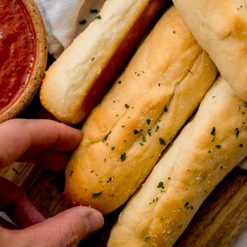 Someone is grabbing a homemade garlic breadstick from a cutting board.