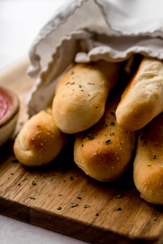 A bunch of garlic breadsticks wrapped in a kitchen towel on a cutting board.