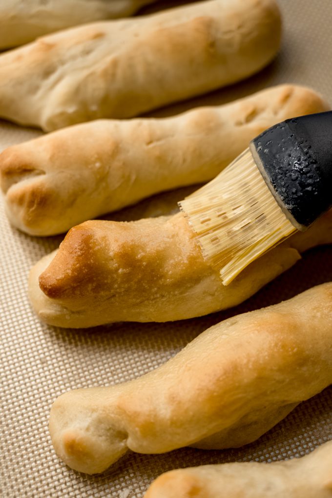 Someone is brushing a homemade garlic breadstick with garlic butter.